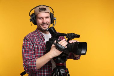 Profesyonel kamera ve turuncu arka planda kulaklığı olan bir adam.