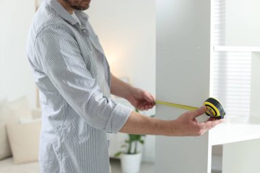 Beyaz rafları bantla ölçen adam içeride, yakın plan.