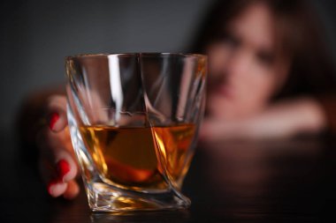 Alkol bağımlılığı. Ahşap masada bir bardak viskisi olan kadın, seçici bir odak noktası.
