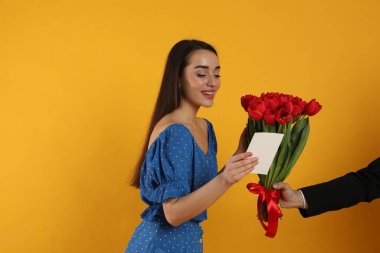Sarı arka plandaki adamdan kırmızı lale buketi alan mutlu kadın. 8 Mart kutlamaları