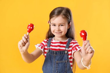 Sarı arka planda oyuncak marakas oynayan tatlı kız.