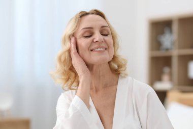 Gülümseyen orta yaşlı kadın evde poz veriyor.