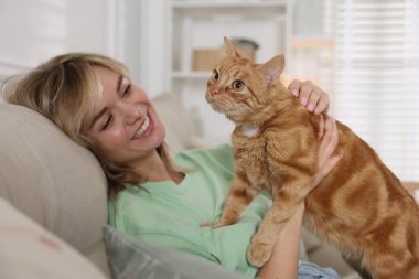 Evdeki kanepede sevimli kızıl kedisi olan bir kadın.