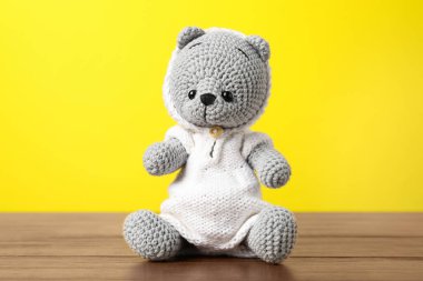 Ahşap masada sarı arka planda sevimli örülmüş oyuncak ayı.