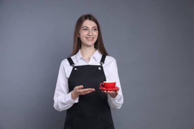 Gri arka planda bir fincan sıcak içecekle gülümseyen barista.
