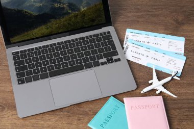 Pasaportlar, uçuş biletleri, uçak modeli ve dizüstü bilgisayar ahşap masanın üstünde.