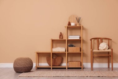 İçerideki bej duvarın yanında dekor, sandalye ve puf bulunan raf ünitesi.