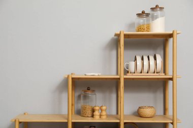 Açık gri duvarın yanında farklı dekorasyona sahip ahşap raf ünitesi.