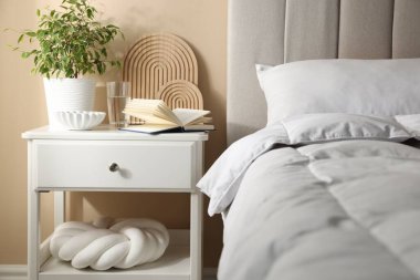 Yatağın yanında kitap, dekor ve bir bardak su olan komodin.