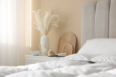 Yatağın yanında kitap, dekor ve bir bardak su olan komodin.