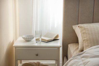 Yatağın yanında kitap, kase ve bir bardak su olan komodinin yanında.