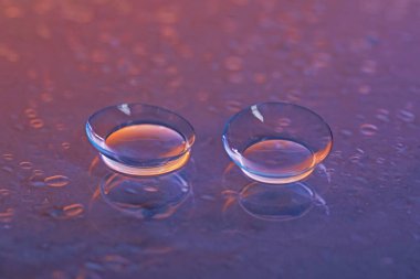 Bir çift kontakt lens ve su damlası mor ayna yüzeyine düşer, yakın plan.