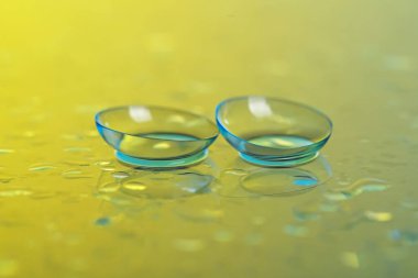 Sarı ayna yüzeyine bir çift kontakt lens ve su damlası, yakın plan.