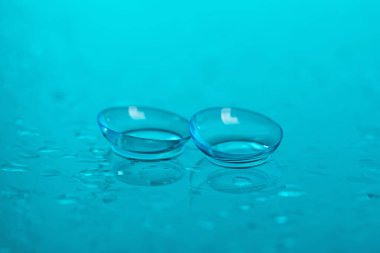 Açık mavi ayna yüzeyine bir çift kontak lens ve su damlası, yakın plan.