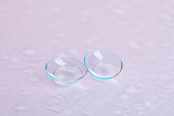 Pair of contact lenses and water drops on light mirror surface, closeup