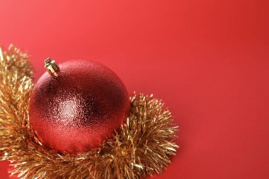 Beautiful Christmas ball and shiny tinsel on red background, closeup. Space for text
