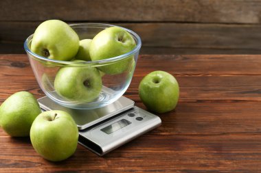 Elektronik mutfak terazisi ve ahşap masada bir kase yeşil elma, yakın plan. Metin için boşluk
