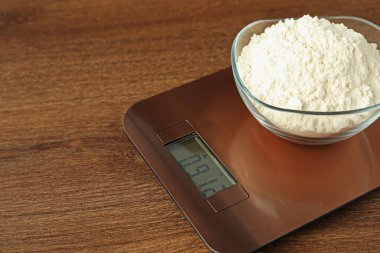 Modern electronic kitchen scale with bowl of flour on wooden table, closeup. Space for text