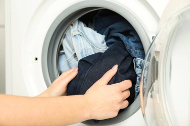 Kadın çamaşır makinesine kot pantolon koyuyor, yakın plan.