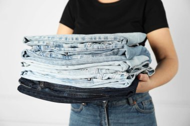 Kapalı alandaki aydınlık duvarın yanında farklı şık kot pantolonları olan kadın, yakın plan.