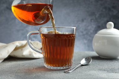 Gri masada çaydanlıktan fincana taze demlenmiş çay dökülüyor, yakın plan.