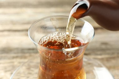 Ahşap masada çaydanlıktan bardağa aromatik çay dökülüyor, yakın plan.