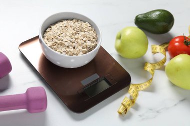 Elektronik mutfak terazisi, mezura, halterler ve ürünler beyaz mermer masaya, yakın çekim. Diyet