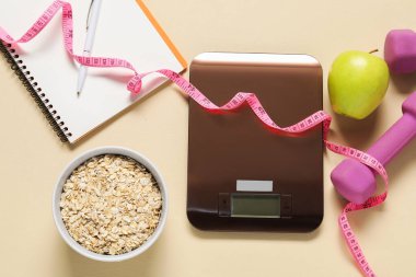 Elektronik mutfak terazisi, mezuralar, dambıllar, not defterleri ve bej masadaki ürünler, düz yatak. Kalori kontrolü