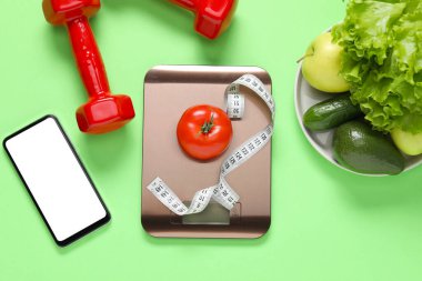 Elektronik mutfak ölçeği, mezura, dambıl, akıllı telefon ve açık yeşil arka plandaki ürünler, düz yatak. Diyet