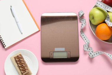 Elektronik mutfak ölçeği, mezura, not defteri ve pembe arka plandaki ürünler, düz konum. Kalori kontrolü