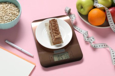 Elektronik mutfak ölçeği, mezura, pembe arka planda kalem ve ürünler. Kalori kontrolü