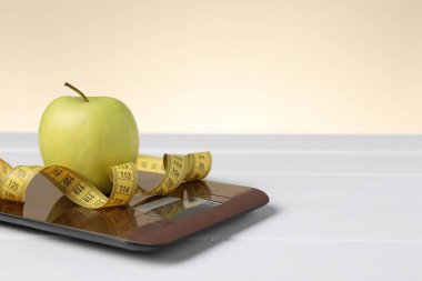 Elektronik mutfak terazisi, beyaz ahşap masa üzerindeki şerit ve elma bej arka planda, yakın plan. Metin için boşluk