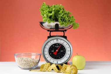 Ürünlerle birlikte mekanik mutfak terazisi ve mercan zeminine karşı beyaz ahşap masadaki şerit. Diyet