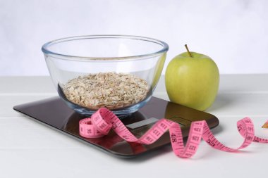 Beyaz ahşap masada yulaf ezmesi, elma ve mezura ile tartılar, yakın plan.