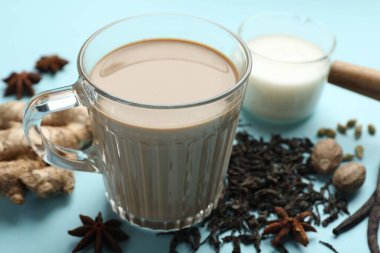 Cam fincanda Aromatik Masala çayı, baharatlar, kuru yapraklar ve açık mavi arka planda süt, yakın plan