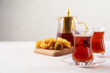 Geleneksel cam bardaklarda Türk çayı, çaydanlık ve beyaz masada taze baklava, yakın plan. Metin için boşluk