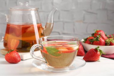 Aromatik meyve çayı, çilek ve nane şekeri beyaz masada, yakın plan.