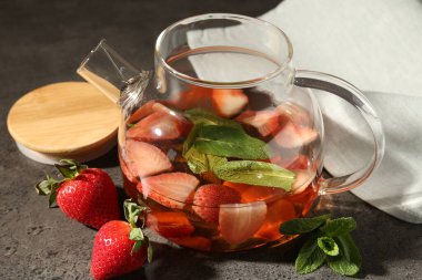 Gri masada aromatik meyve çayı, çilek ve nane içeren cam çaydanlık, yakın plan.
