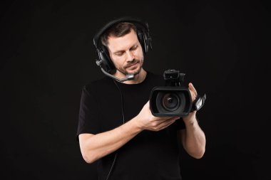 Profesyonel kameralı ve kulaklıklı bir adam siyah arka planda.