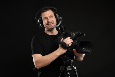 Profesyonel kameralı ve kulaklıklı bir adam siyah arka planda.