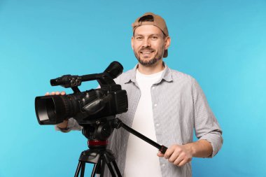 Açık mavi arka planda profesyonel video kamerası olan adam.
