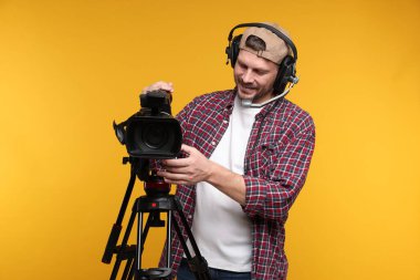 Profesyonel kamera ve turuncu arka planda kulaklığı olan bir adam.