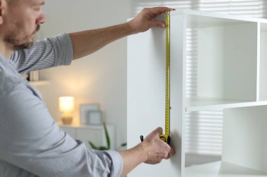 Beyaz rafları bantla ölçen adam içeride, yakın plan.