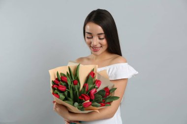 Açık gri arka planda kırmızı lale çiçekli mutlu kadın. 8 Mart kutlamaları