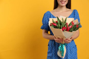 Sarı arka planda kırmızı lale çiçekleri olan mutlu kadının yakın görüntüsü, mesaj için yer var. 8 Mart kutlamaları