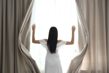 Evde perdeleri açan kadın, arka manzara