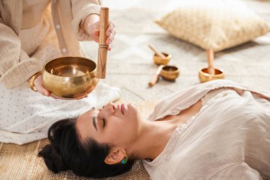 Şarkı söyleyen kadın kase terapisi görüyor. Kapalı yerde yatıyor.