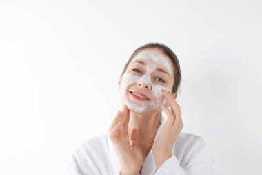 Spa günü. Güzel bir kadın beyaz arka planda yüzüne maske takıyor.