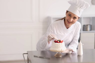 Pastacı mutfakta taze böğürtlenlerle pasta süslüyor.