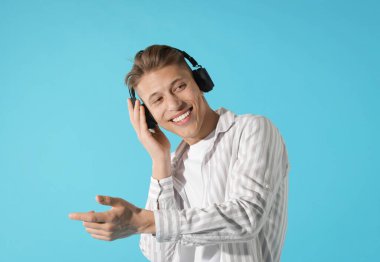 Kulaklıklı mutlu adam açık mavi arka planda dans ediyor.